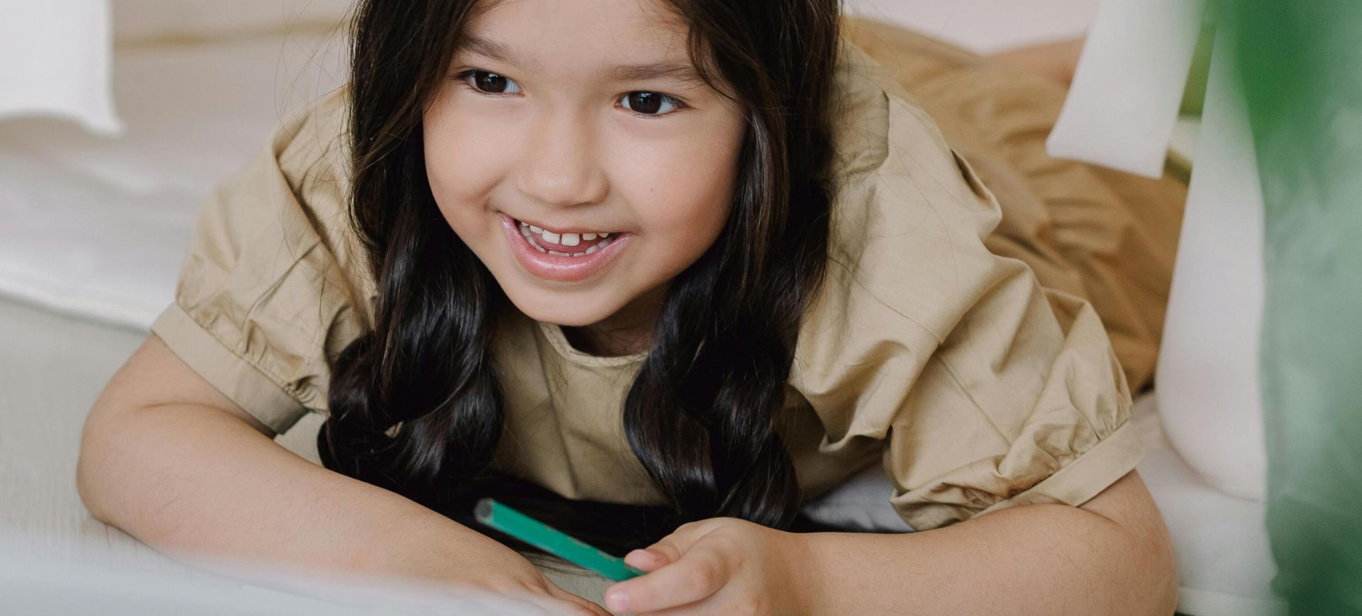 Cute Asian girl smiling while using a laptop for her online class, showcasing joyful learning.